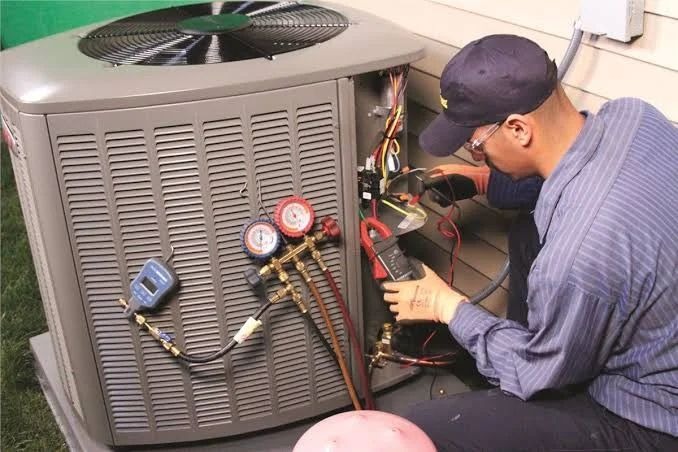 HVAC technician inspecting outdoor central air conditioning unit with gauges